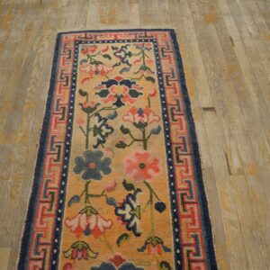 Yellow and pink floral runner with blue fret border sits on distressed wood plank flooring.
