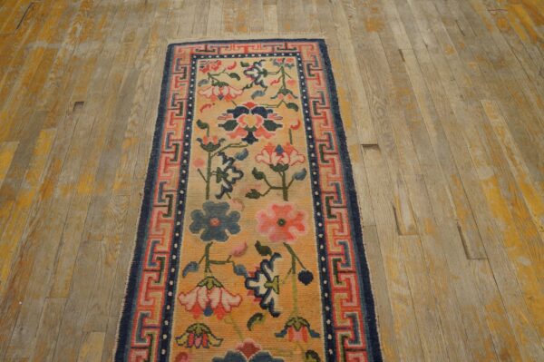 Yellow and pink floral runner with blue fret border sits on distressed wood plank flooring.