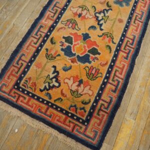 Gold rug with colorful floral motifs and a complex blue and red geometric border on worn wood.