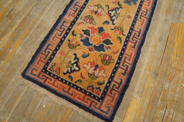 Gold rug with colorful floral motifs and a complex blue and red geometric border on worn wood.