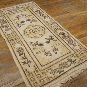 Low-pile beige rug displaying floral and complex geometric motifs on worn wood flooring.