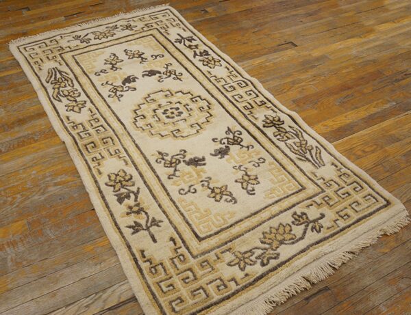 Low-pile beige rug displaying floral and complex geometric motifs on worn wood flooring.