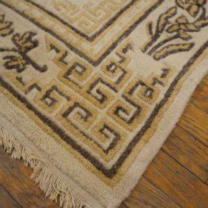 Beige rug with dark brown and yellow geometric border and floral designs on rustic wood flooring.