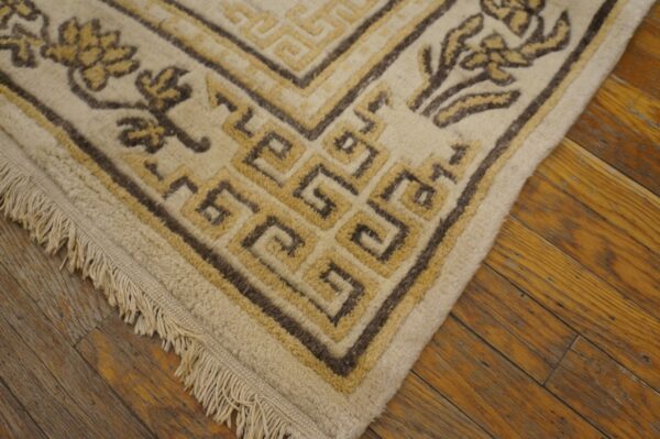 Beige rug with dark brown and yellow geometric border and floral designs on rustic wood flooring.