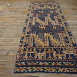 Narrow blue runner rug with geometric gold and rust tribal motifs on distressed wood flooring.