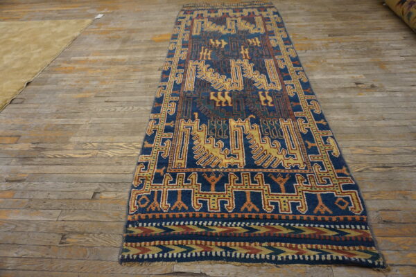 Narrow blue runner rug with geometric gold and rust tribal motifs on distressed wood flooring.