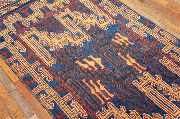 Deep blue rug with contrasting yellow and red tribal motifs sits on weathered wood flooring.