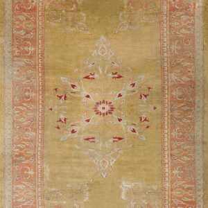 Low-pile rug in golden green with a red and cream central design and a floral salmon pink border.