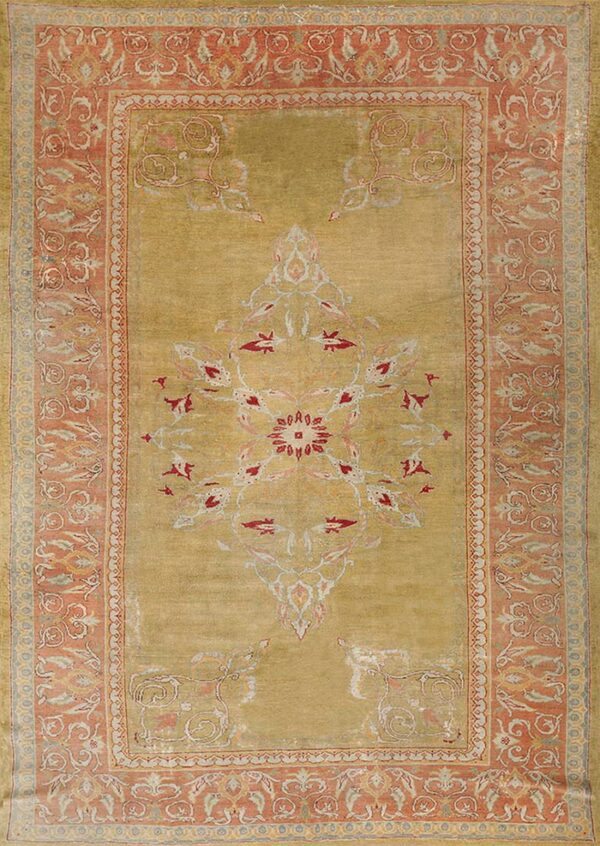 Low-pile rug in golden green with a red and cream central design and a floral salmon pink border.