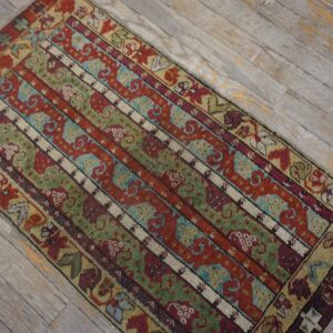 Low-pile rug with geometric striped patterns in red, green, teal, and burgundy on distressed light wood planks.