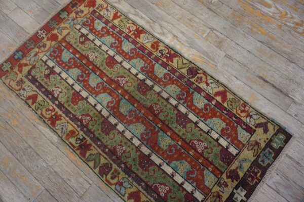 Low-pile rug with geometric striped patterns in red, green, teal, and burgundy on distressed light wood planks.
