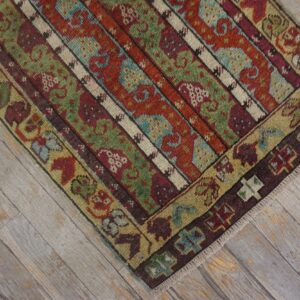 Low-pile rug in rust, sage, and blue stripes with detailed borders rests on distressed gray wood planks.