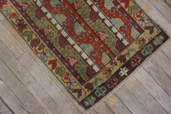 Low-pile rug in rust, sage, and blue stripes with detailed borders rests on distressed gray wood planks.