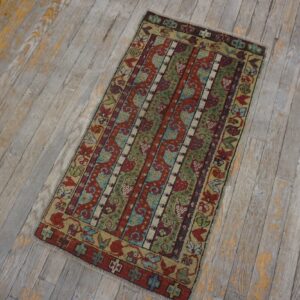 A colorful tribal rug with red, green, and blue stripes rests on weathered gray wood flooring.