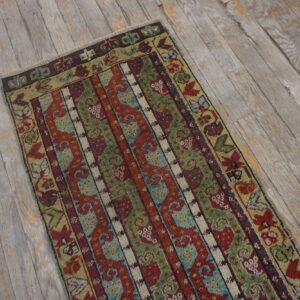 Striped runner rug in deep red, olive green, and blue patterns on distressed gray plank flooring.