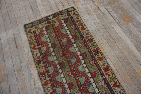 Striped runner rug in deep red, olive green, and blue patterns on distressed gray plank flooring.
