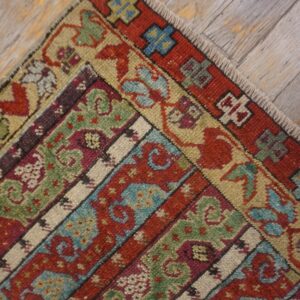 Low pile rug corner displaying red, green, and blue banded traditional patterns on weathered gray wood planks.