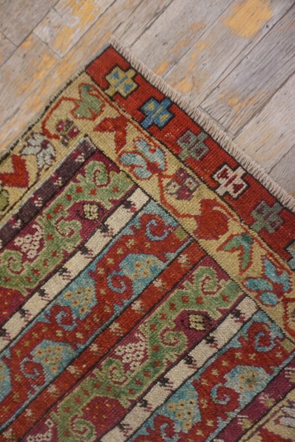 Low pile rug corner displaying red, green, and blue banded traditional patterns on weathered gray wood planks.