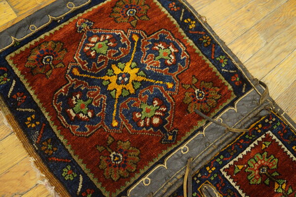 Rustic red and blue geometric rug attached to dark leather, resting on light wooden planks.