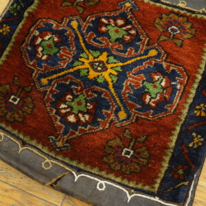 High-pile red and navy rug with geometric motifs and a leather stitched backing rests on distressed wood flooring.