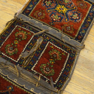 A detailed red and navy patterned textile saddlebag with dark leather trim rests on light wood floors.