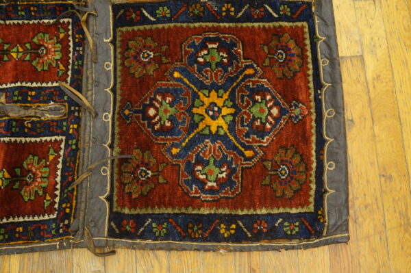 Rust and blue patterned textile fragment with leather trim and straps resting on light wood flooring.
