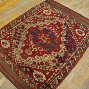 Geometric red and blue rug with complex borders on distressed, yellow-toned hardwood flooring.