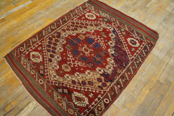 Geometric red and blue rug with complex borders on distressed, yellow-toned hardwood flooring.