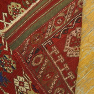 Red rug with traditional geometric patterns and striped green borders rests on yellow wood flooring.