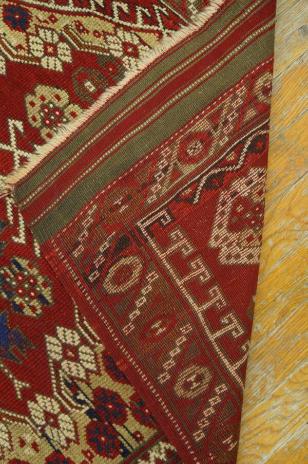 Red rug with traditional geometric patterns and striped green borders rests on yellow wood flooring.