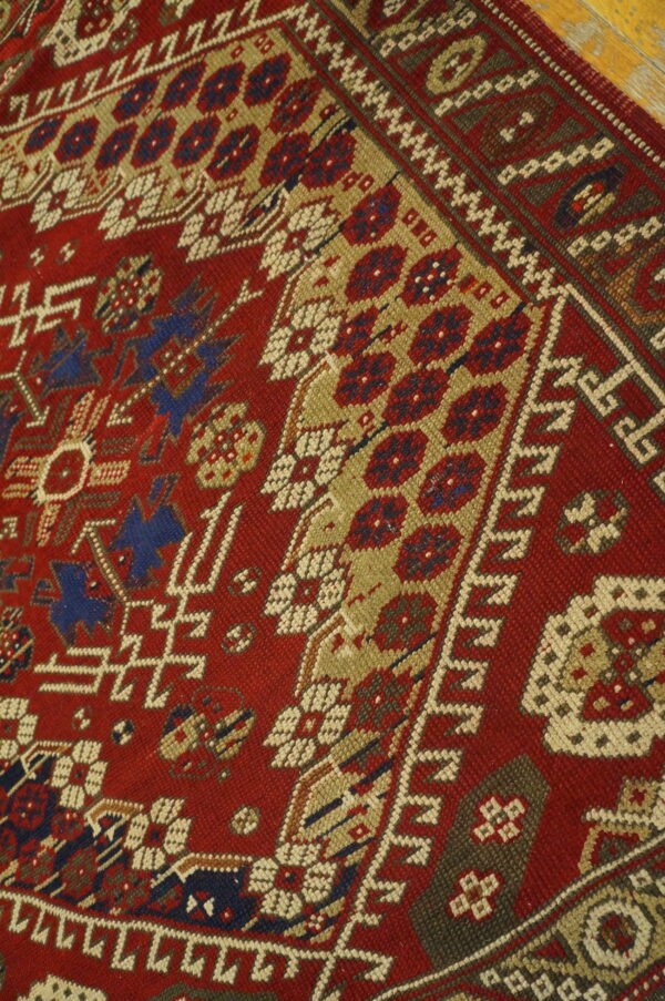 Geometric patterns in red, tan, navy, and cream dominate this low-pile rug lying on a wood floor.