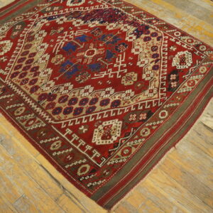 Geometric red rug with blue and tan tribal motifs placed on worn, light-colored wooden floor planks.