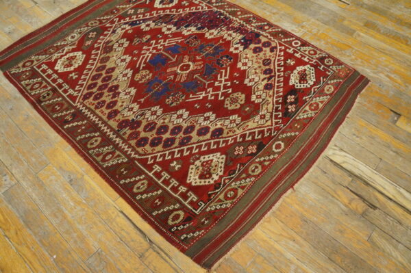 Geometric red rug with blue and tan tribal motifs placed on worn, light-colored wooden floor planks.