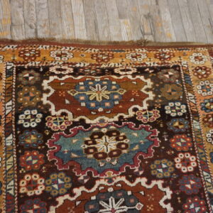 A deeply colored patterned rug with dark brown, teal, and gold accents rests on distressed gray wood flooring.