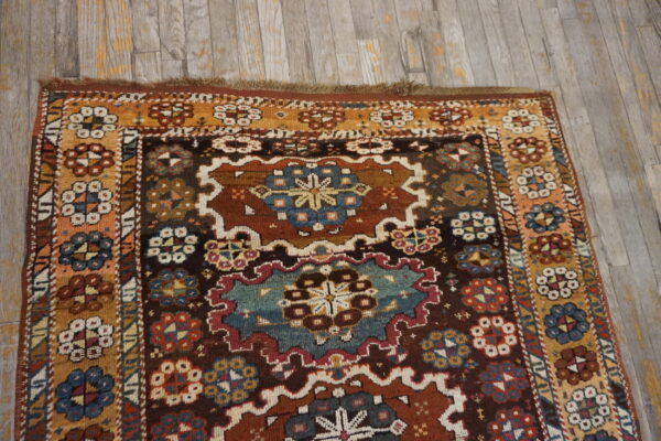 A deeply colored patterned rug with dark brown, teal, and gold accents rests on distressed gray wood flooring.