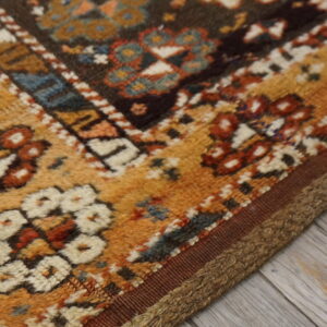 Geometric rug pattern in mustard, rust, cream, and blue lies on gray weathered wood flooring.