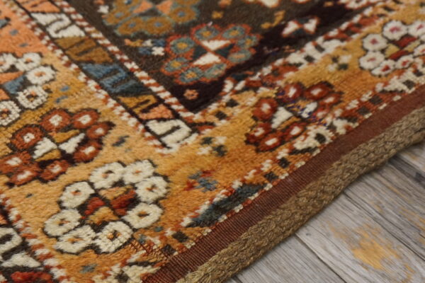 Geometric rug pattern in mustard, rust, cream, and blue lies on gray weathered wood flooring.