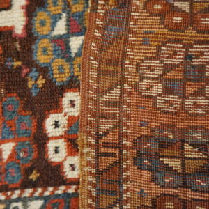 Close-up of a brown piled rug with colorful motifs next to a rust-colored geometric flatweave textile.