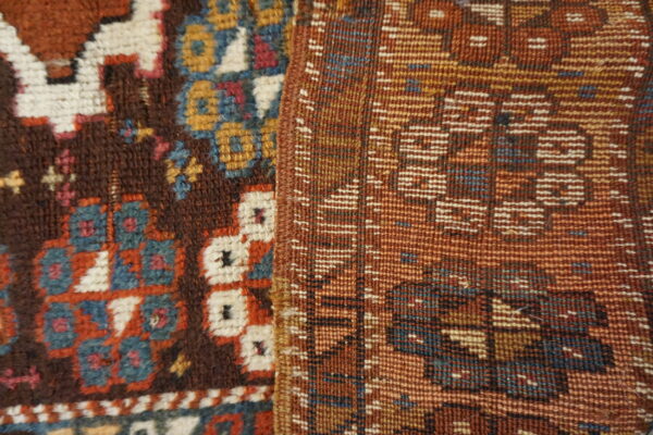Close-up of a brown piled rug with colorful motifs next to a rust-colored geometric flatweave textile.