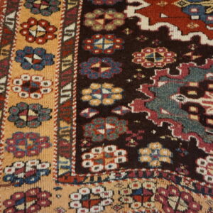 Close-up of a tribal rug with intricate floral and geometric patterns in deep red, teal, black, and peach on wood flooring.
