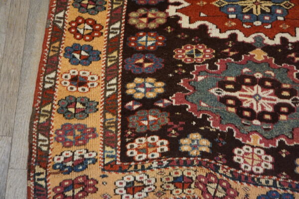 Close-up of a tribal rug with intricate floral and geometric patterns in deep red, teal, black, and peach on wood flooring.