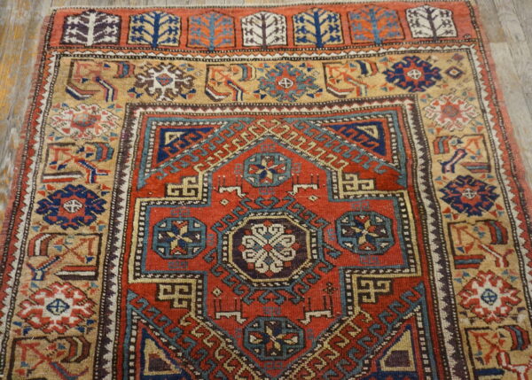 Red and navy geometric rug with a tan border sits on a weathered light brown wooden floor.