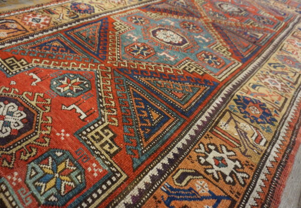 Geometric patterned rug with a main field of terracotta red, blue, and teal on wooden flooring.
