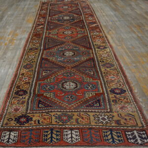 Red and navy geometric runner with tan accents on distressed gray and yellow plank flooring.