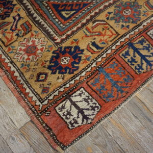 Rust, navy, and gold low-pile rug with stylized geometric patterns rests on gray distressed wood floor.