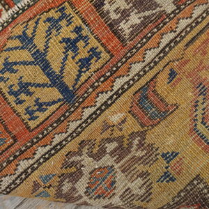 A tightly woven rug with orange, mustard, and blue geometric patterns rests on light wood planks.