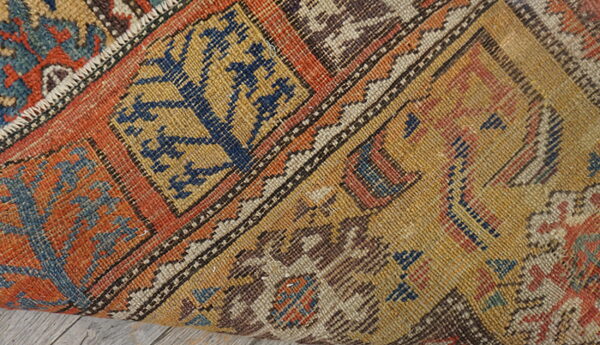 A tightly woven rug with orange, mustard, and blue geometric patterns rests on light wood planks.