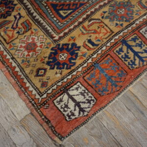Rustic geometric rug featuring tan, terracotta, and navy patterns on weathered gray wood flooring.