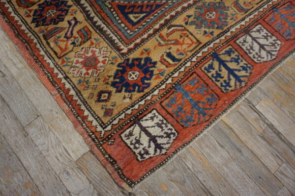 Rustic geometric rug featuring tan, terracotta, and navy patterns on weathered gray wood flooring.