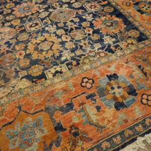 Blue and rust patterned rug with dense floral motifs and fringes lying on light wood planks.
